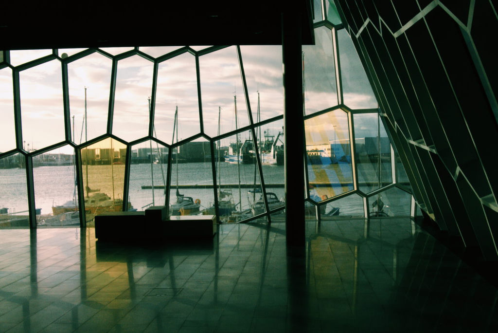 The inside of a hall with honeycomb-like, floor stop ceiling windows overlooking a harbour with many docked sailboats.