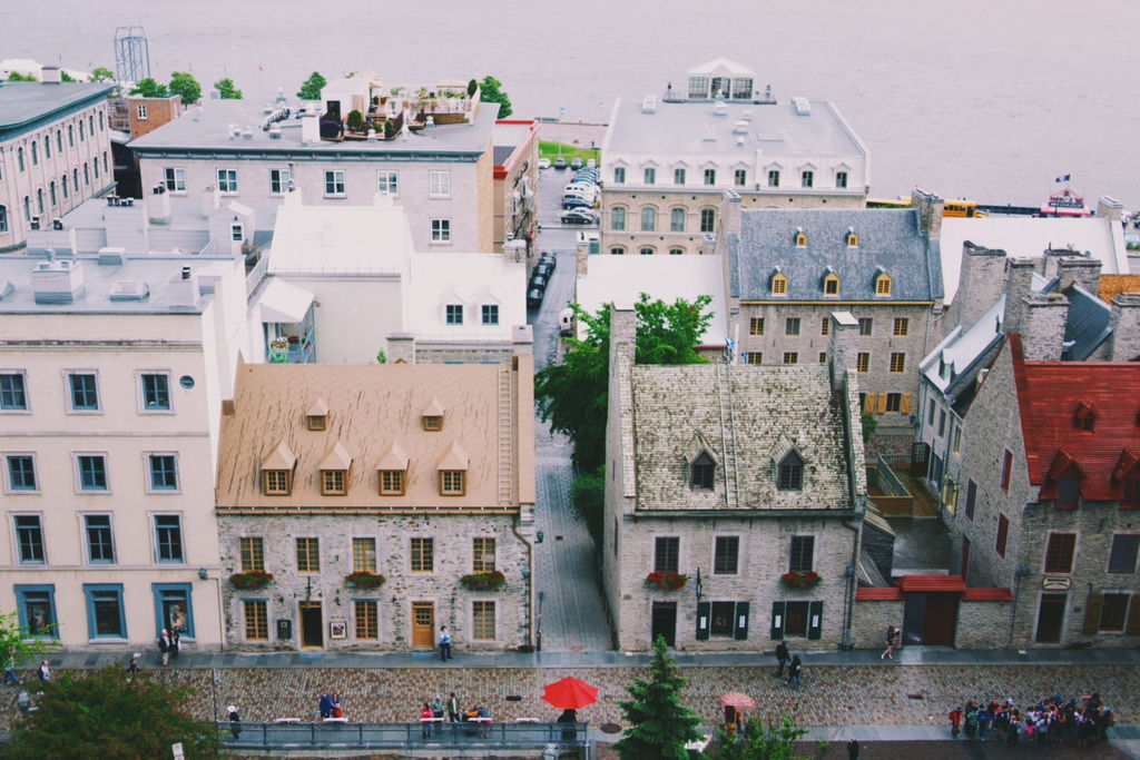 Old buildings in old Quebec as seen from a higher point  with people along the street, with one stood out, standing under a red umbrella.