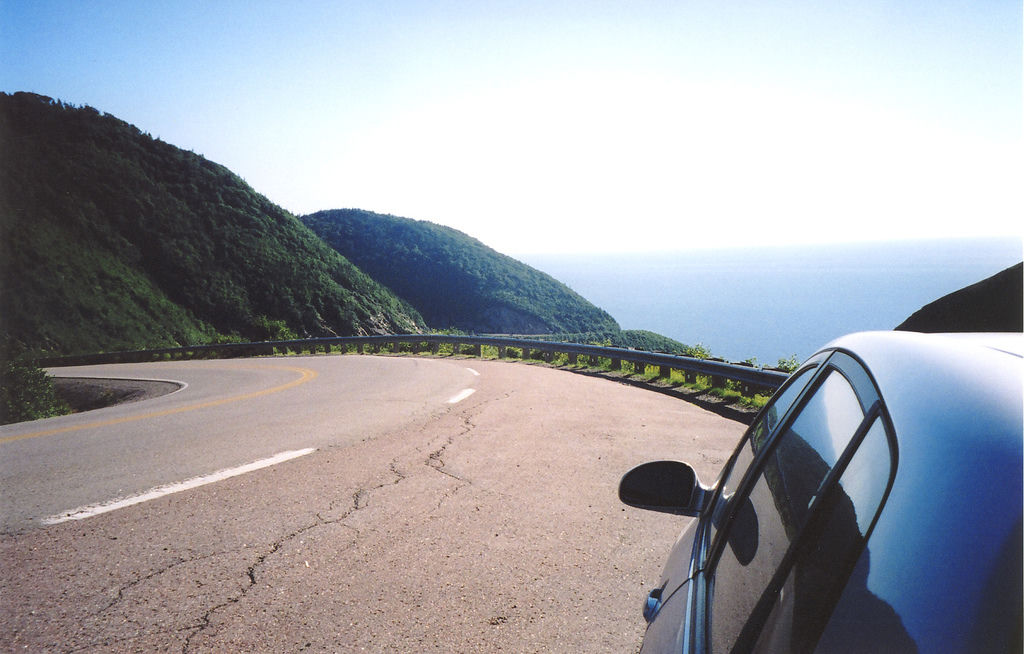 A scenic road with the ocean at the end of it and glorious skies reflected on the shiny car.