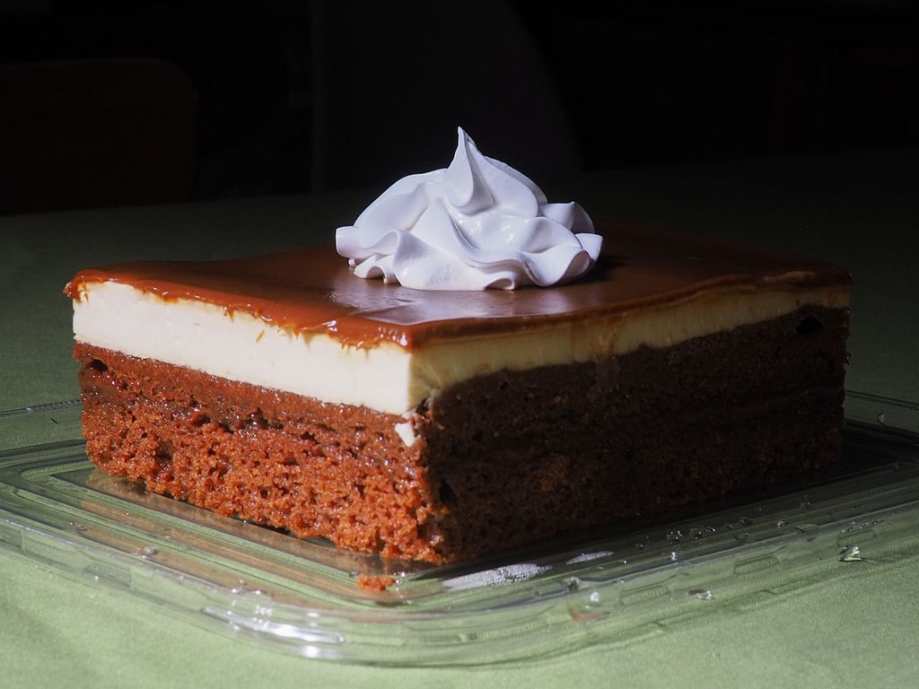 A rectangular, brown cake with a small dollop of whipping cream on top.