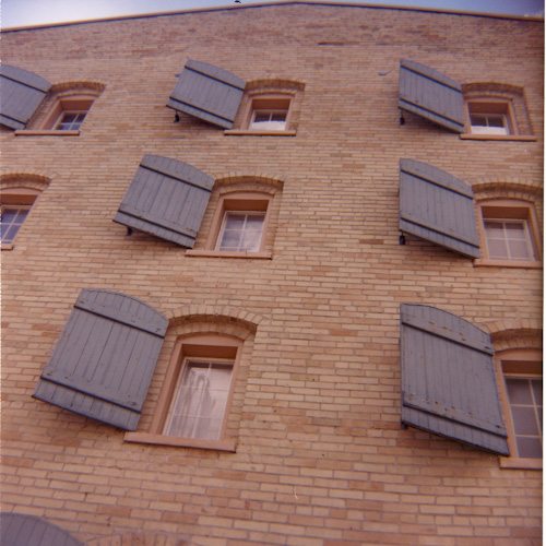 A close-up photo of a yellow brick building with light blue window shutters.