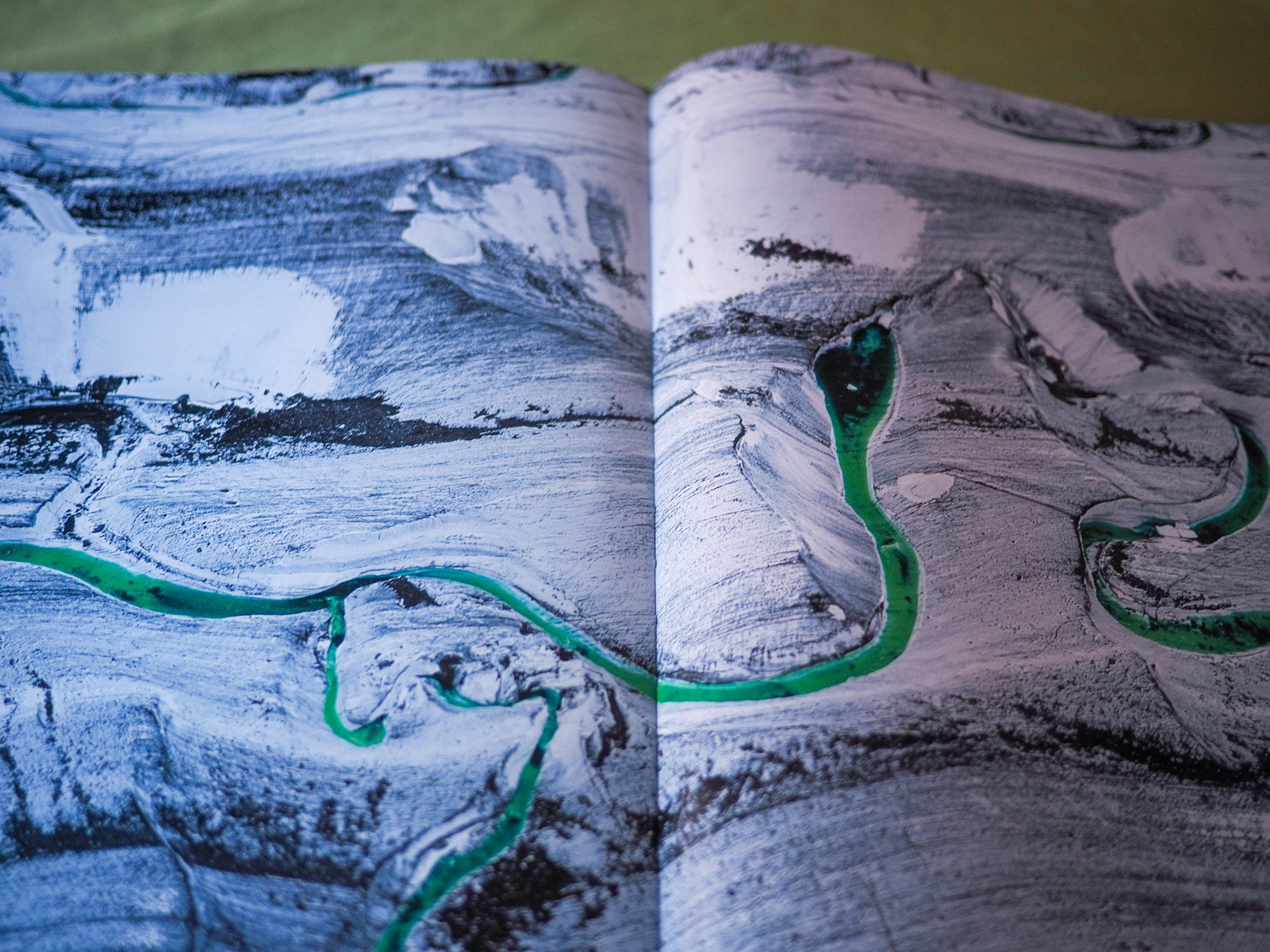 A two-page spread of an aerial photo of a glacial river in a snowy, mountain landscape.